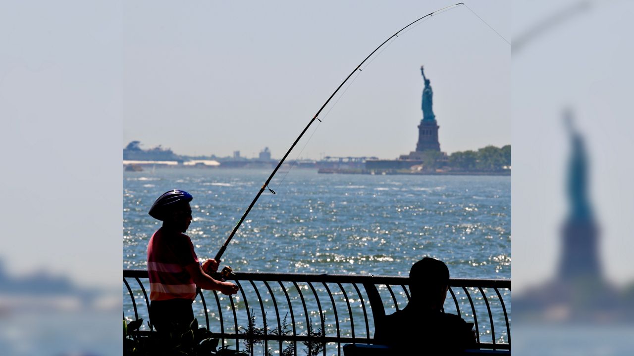 People fishing from a railing with the Statue of Liberty in the distance
